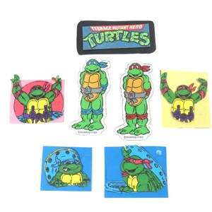 May include: Set of seven Teenage Mutant Ninja Turtles stickers. The stickers feature the Teenage Mutant Ninja Turtles characters in various poses and settings. The stickers are printed on white paper with a glossy finish. The stickers are approximately 2 inches in diameter.
