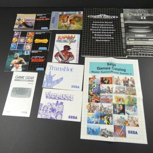 May include: A collection of Sega video game manuals and a game catalog. The manuals include titles like RHAMY, Boxing, TransBot, Vigilante, and Game Gear. The catalog features a grid of game screenshots and the text "Sega Games Catalog Master System/Master System II".