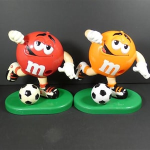 1 Dispensador de M&M vintage de fútbol con diseño de caramelos naranjas o rojos, personajes de chocolate Marc Inc.