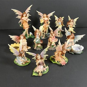 Könnte beinhalten: Eine Sammlung von Feenfiguren mit detaillierten Flügeln und fließenden Kleidern. Die Feen sind in verschiedenen Posen, einige stehen und andere sitzen, mit Farben wie Rosa, Gelb und Grün. Die Figuren sind aus glänzendem Material.