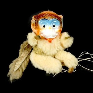 May include: A vintage hand puppet monkey with a white fur body, brown and orange face, and blue eyes. The puppet has strings attached to its limbs and a tail.
