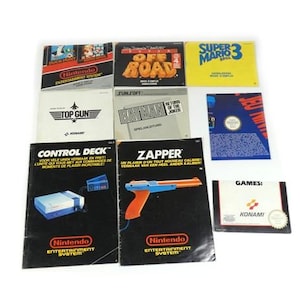 May include: A collection of Nintendo Entertainment System instruction manuals and game booklets, including titles like Super Mario Bros. 3, Top Gun, Batman, and Off Road, alongside a Zapper light gun manual and a Konami games pamphlet.