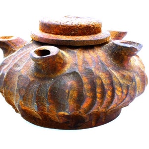 May include: A rustic, brown ceramic teapot with a lid and multiple spouts. The teapot has a textured, uneven surface and appears to be aged or weathered.