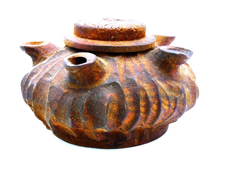 May include: A rustic, brown ceramic teapot with a lid and multiple spouts. The teapot has a textured, uneven surface and appears to be aged or weathered.