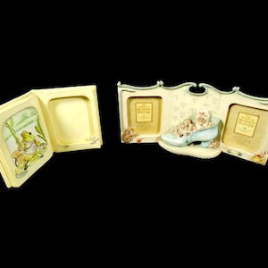 May include: A white picture frame with a book design. The frame has three openings, one with a frog illustration and two with the text "The World of Beatrix Potter".