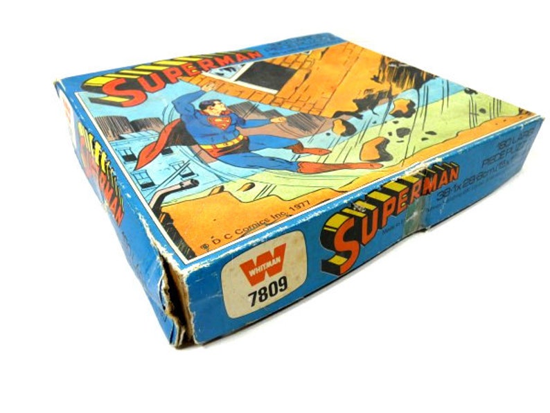May include: A vintage Superman board game box with a blue background and a picture of Superman flying. The box has the text "Superman" and "Whitman" on it. The box is in good condition with some wear and tear.