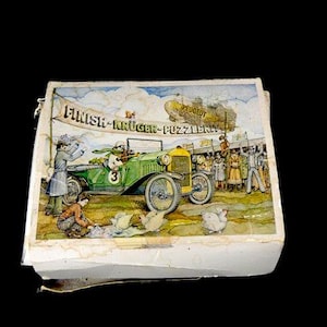 May include: Vintage puzzle box depicting a green racing car with the number 3, approaching a finish line banner. The banner reads "FINISH-KRUGER-PUZZLERNA". A yellow Peugeot airship is in the background.