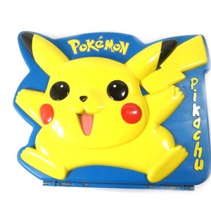 May include: A blue and yellow plastic lunchbox featuring a cartoon image of Pikachu, a popular Pokemon character. The lunchbox has the words "Pokemon" and "Pikachu" printed on it.