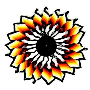 May include: A colorful crocheted sun catcher with a black center. The sun catcher is made of white, yellow, orange, and red yarn.