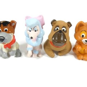Könnte beinhalten: Satz mit vier Plastikfiguren von Cartoon-Hunden und einer Katze. Die Figuren sind braun, grau, weiß und orange. Die Hunde tragen rote Halsbänder. Die Katze trägt ein rotes Halsband mit einer Glocke.