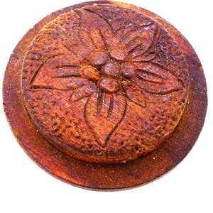 May include: A round wooden bottle stopper with a carved floral design. The stopper is a dark brown color and has a smooth, polished finish.