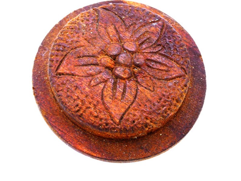 May include: A round wooden bottle stopper with a carved floral design. The stopper is a dark brown color and has a smooth, polished finish.