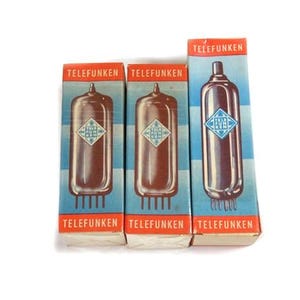 Puede incluir: Tres válvulas de vacío Telefunken vintage en sus cajas originales. Las cajas son azules y naranjas con el logotipo de Telefunken e ilustraciones de tubos. Las válvulas son marrones y plateadas, con un logotipo en forma de diamante.
