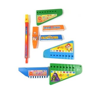 May include: A set of eight colorful plastic toy musical instruments. The instruments include a recorder, a whistle, and six harmonicas. The harmonicas feature different cartoon characters and musical notes.