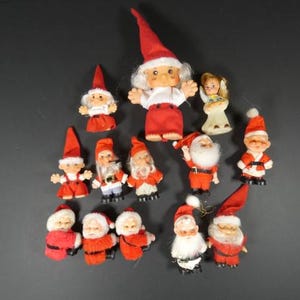 May include: A collection of vintage Christmas figurines, including Santa Claus, elves, and an angel. The figurines are primarily red and white, with some featuring black accents. The figures are made of plastic and fabric.
