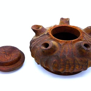 May include: A brown ceramic lidded jar with a textured surface and multiple holes around the top. The lid has a carved design.