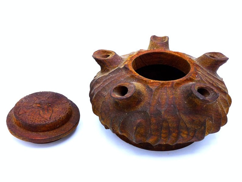 May include: A brown ceramic lidded jar with a textured surface and multiple holes around the top. The lid has a carved design.