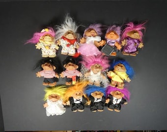 May include: A collection of thirteen troll dolls with various hair colors including pink, white, purple, blue, yellow, and orange. The dolls are dressed in diverse outfits such as dresses, pirate shirts, formal suits, and casual clothing items.