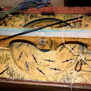 May include: Vintage wooden fishing game with a painted landscape scene. The game features a rotating disc with fish cutouts, a black fishing rod, and a brick border. A bundle of dried lavender rests on top.