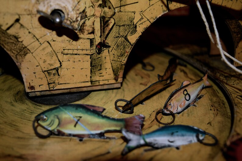May include: Close-up of a vintage toy with a yellow and brown painted background. The toy features several fish with numbers 7 and 8, and a winding key. The fish have metal rings attached.