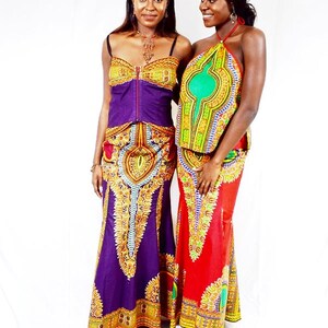 May include: Two women wearing colourful maxi skirts with intricate patterns and matching tops. The skirt on the left is purple with gold accents, while the skirt on the right is red with gold and green accents.