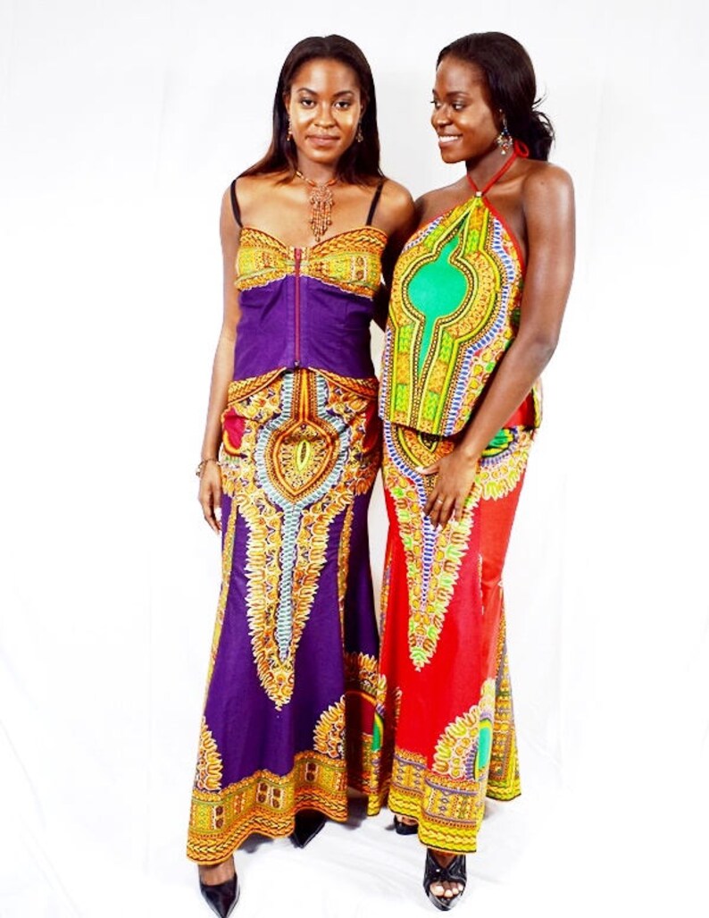 May include: Two women wearing colourful maxi skirts with intricate patterns and matching tops. The skirt on the left is purple with gold accents, while the skirt on the right is red with gold and green accents.