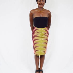 Puede incluir: Una mujer con un top negro sin tirantes y una falda estampada en rojo y dorado. Lleva un collar dorado y tacones negros.