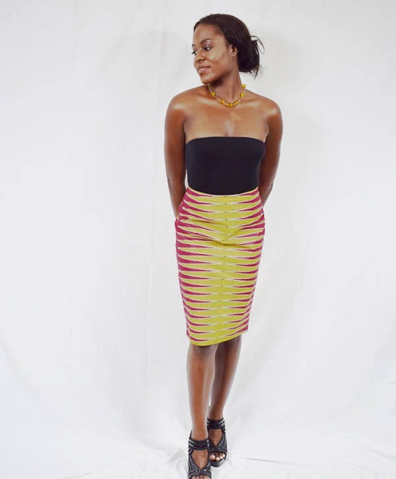 Puede incluir: Una mujer con un top negro sin tirantes y una falda l&aacute;piz de estampado amarillo y burdeos. Lleva un collar dorado y tacones negros.