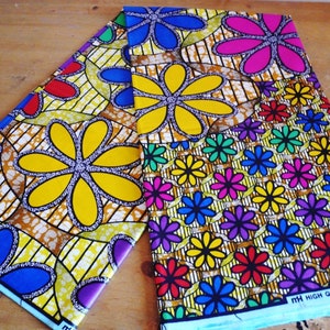 May include: Two pieces of colorful fabric with a floral pattern. The fabric has a yellow background with blue, red, green, purple, and pink flowers. The fabric is printed with the text "HIGH QUALITY JAVA PRINT".