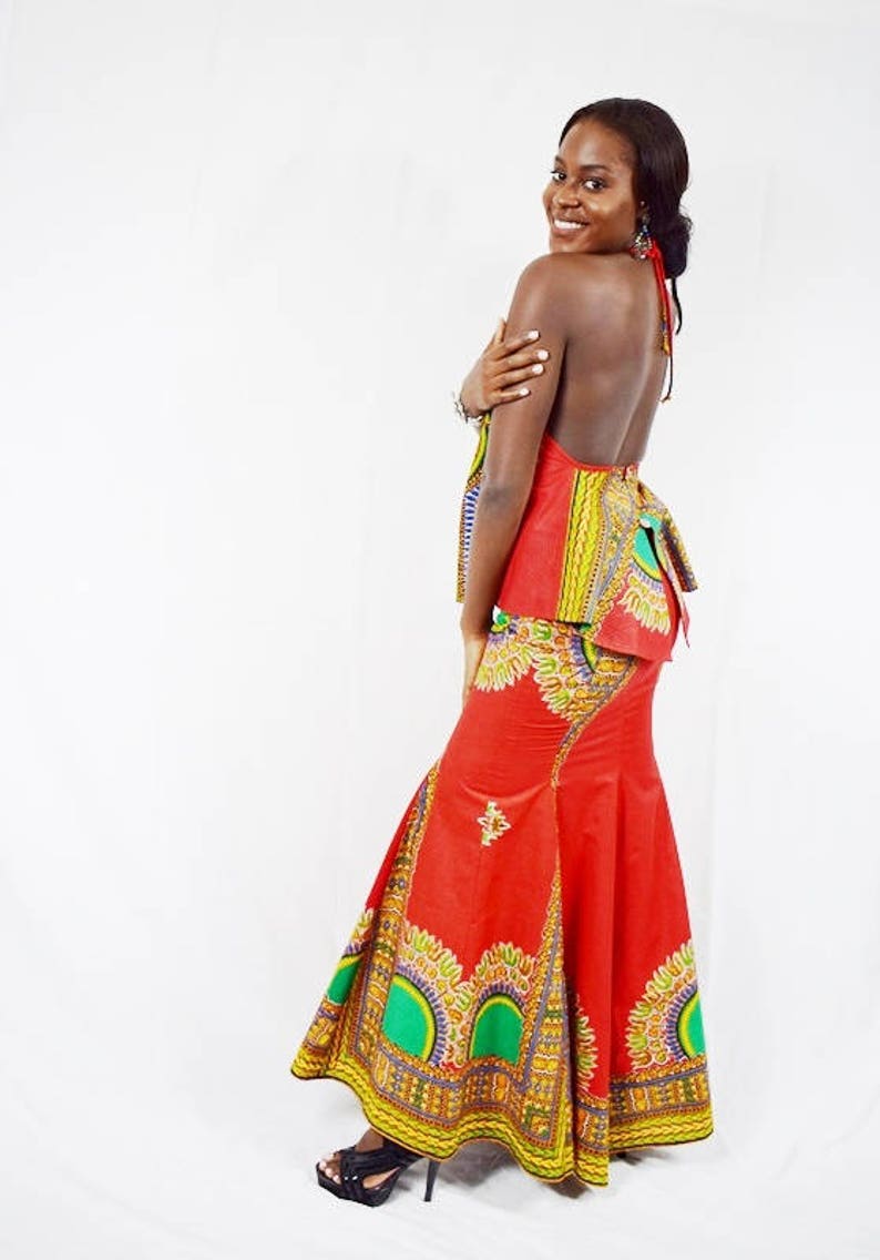 May include: A woman wearing a red and green patterned maxi skirt with a matching halter top. The skirt has a mermaid style hemline and the top has a halter neckline.