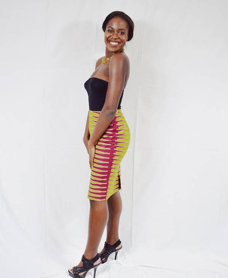 Puede incluir: Una mujer con un top negro sin tirantes y una falda l&aacute;piz amarilla y burdeos con una abertura lateral. Lleva tacones negros y sonr&iacute;e.