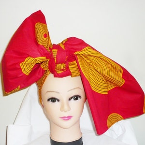 May include: A red and yellow patterned head wrap tied in a large bow. The wrap is made of fabric with a geometric design.
