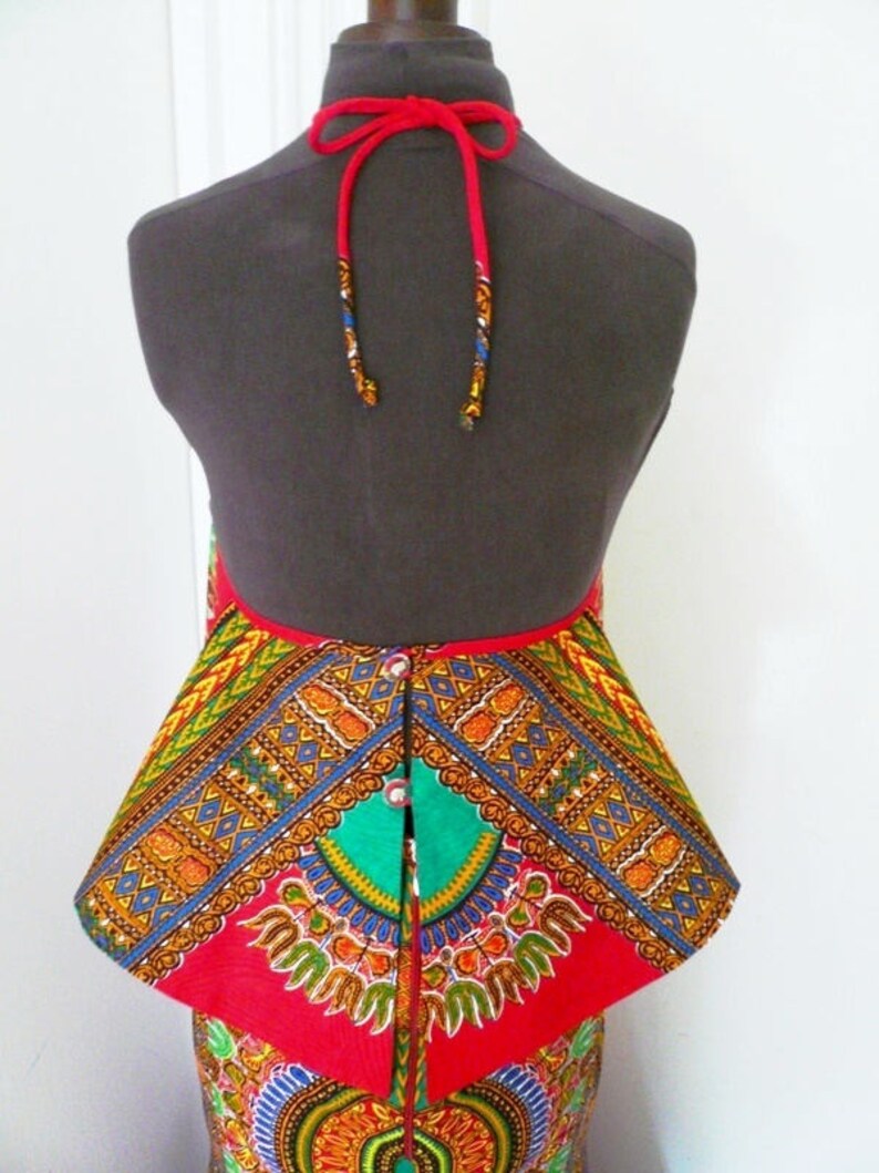 May include: A red and green patterned skirt with a red peplum top. The top has a halter neck with red ties. The skirt and top are made of African print fabric.