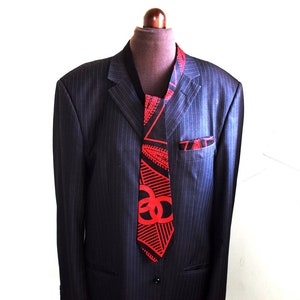 May include: A black suit jacket with a red and black patterned tie. The tie has a geometric design with red triangles and black lines.