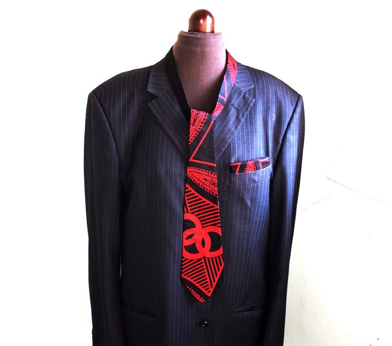 May include: A black suit jacket with a red and black patterned tie. The tie has a geometric design with red triangles and black lines.