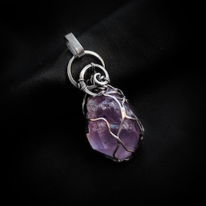 以下が含まれることがあります： 黒い背景に、銀のワイヤーで包まれた紫色のアメジストの結晶。銀製のベイルと銀製のリングが付いています。