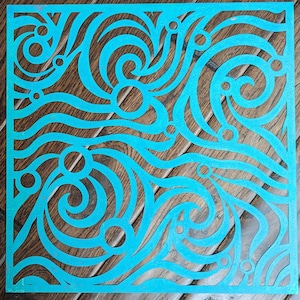 Puede incluir: Una plantilla azul turquesa con un patrón de espiral y círculos. La plantilla está sobre un fondo de madera.