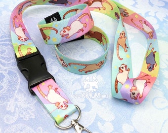 Puede incluir: Un cordón colorido y dos pulseras a juego con un patrón repetido de ratas de dibujos animados sobre un fondo pastel. El cordón tiene un clip de plástico negro y un llavero plateado. Las pulseras son de tela y tienen un patrón de estrellas.