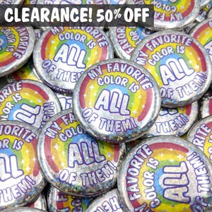 May include: A pile of circular, silver-coloured badges featuring the text "MY FAVORITE COLOR IS ALL OF THEM!" in a rainbow design. The badges have a holographic, glittery effect. The top of the image reads "CLEARANCE! 50% OFF".