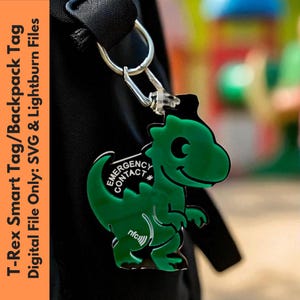 May include: A green T-Rex shaped backpack tag with the words "EMERGENCY CONTACT" and "nfc" printed on it. The tag is attached to a silver keyring. The text "T-Rex Smart Tag/Backpack Tag" is printed on the left side of the image.