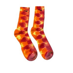May include: A pair of orange and red tie-dye socks with a black Nike swoosh logo on each sock.