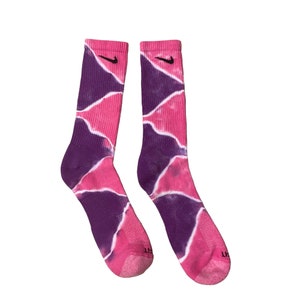 May include: A pair of pink and purple tie-dye socks with a black Nike logo on each sock.