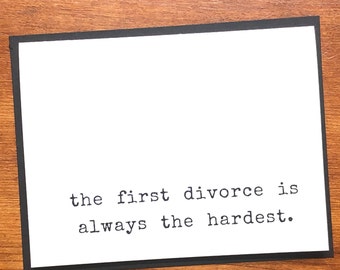 May include: A white card with a black border features the text "the first divorce is always the hardest" in a typewriter font. The card is set against a wooden background.