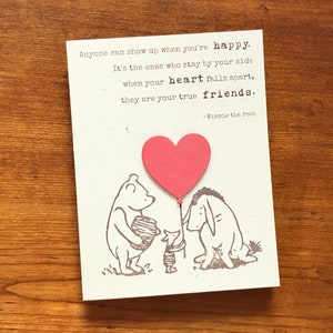 May include: A card with a quote from Winnie the Pooh about friendship. The quote reads: "Anyone can show up when you're happy. It's the ones who stay by your side when your heart falls apart, they are your true friends." -Winnie the Pooh. The card features a pink heart balloon held by Winnie the Pooh and Piglet.