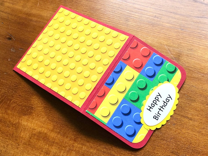 May include: A handmade birthday card with a red border and a yellow interior patterned with raised circles. The right side features a colorful block design, and a yellow scalloped oval with "Happy Birthday" is attached.