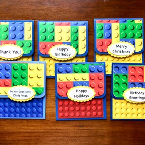 May include: A collection of colorful greeting cards designed to resemble toy building blocks. Each card features a different message, including "Thank You!", "Happy Birthday", "Merry Christmas", "Do Not Open Until Christmas", "Happy Holidays", and "Birthday Greetings".