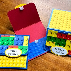 May include: Three handmade greeting cards with a Lego block design. The cards feature yellow, blue, green, and red colors. One card says "Happy Birthday" and another says "Birthday Greetings" on a white oval with a yellow border.