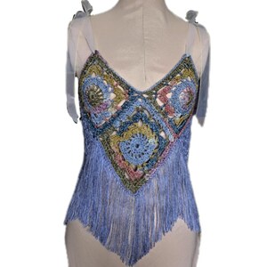 May include: A blue crochet top with a colourful geometric pattern and fringe trim. The top has thin straps and a V-neckline.