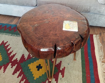 May include: A round wooden table with a natural wood grain finish and a clear epoxy top. The table has three gold hairpin legs and is sitting on a rug with a colorful geometric pattern.