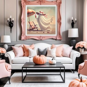 May include: A framed artwork depicts a whimsical ghost enjoying a beach day, wearing a hat and holding an ice cream cone. The artwork is framed in a pink ornate frame, above a white sofa with pink and gray pillows. A black coffee table holds pumpkins.